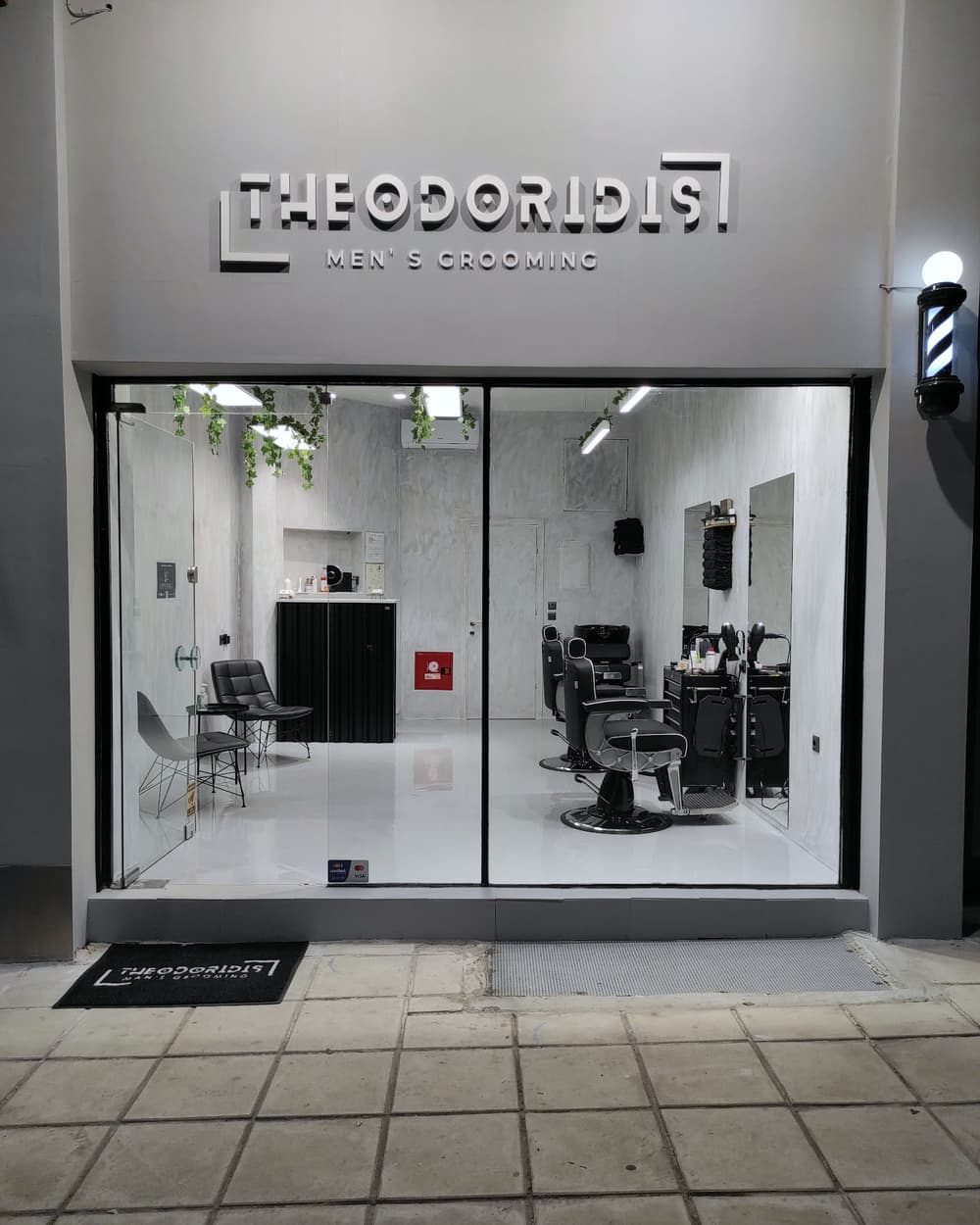 Η πρόσοψη του Theodoridis Men's Grooming το βράδυ, με την ταμπέλα και τον φωτισμένο χώρο