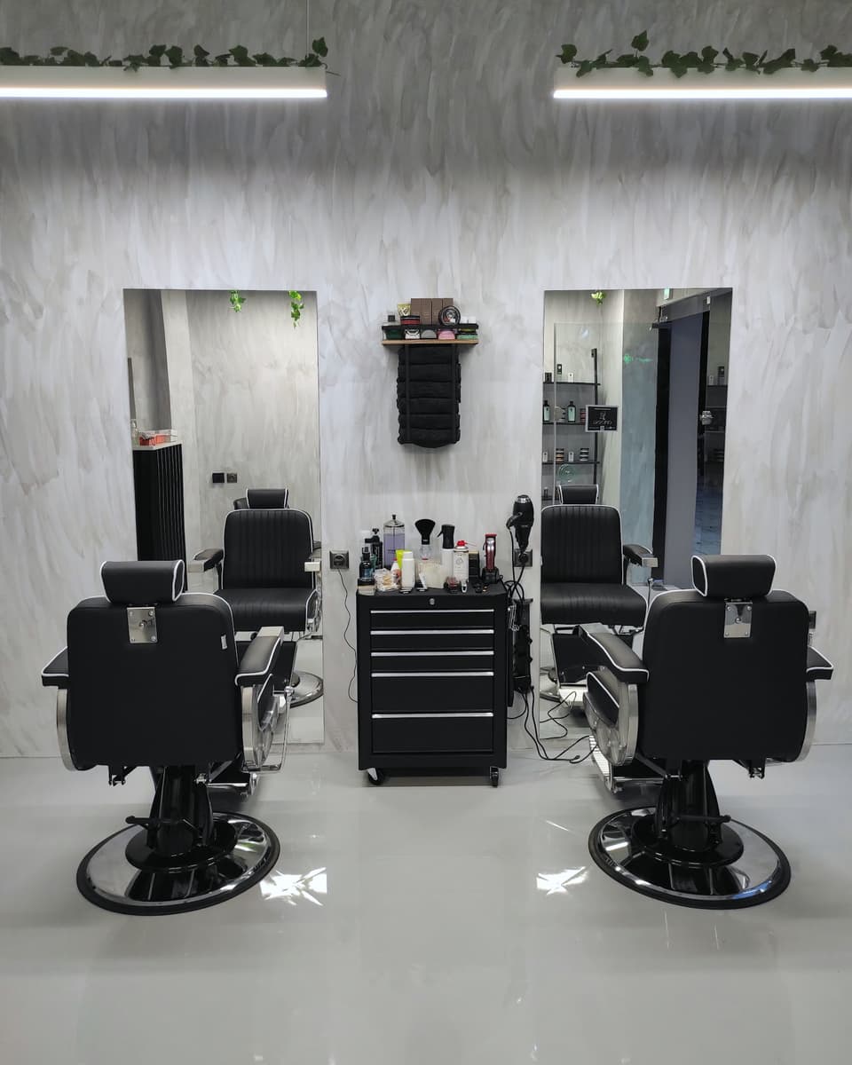 Οι δύο καρέκλες του Theodoridis Men's Grooming μπροστά στον γκρι μαρμάρινο τοίχο, με τα φωτιστικά και τον κισσό